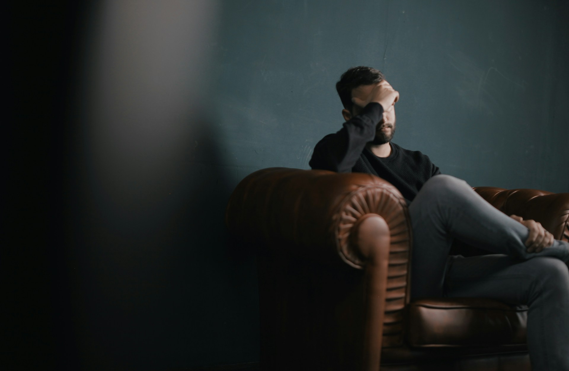 A man holds his head while sitting on a sofa.