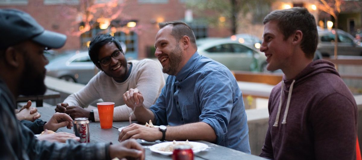 Guys from a dinner group talking around an outdoor table in Hoboken